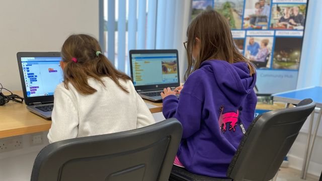 two girls sat at laptops using scratch